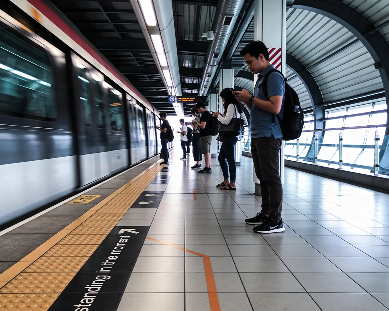 A group of commuters standing along the platform of an MRT station, patiently waiting for the arriving train.