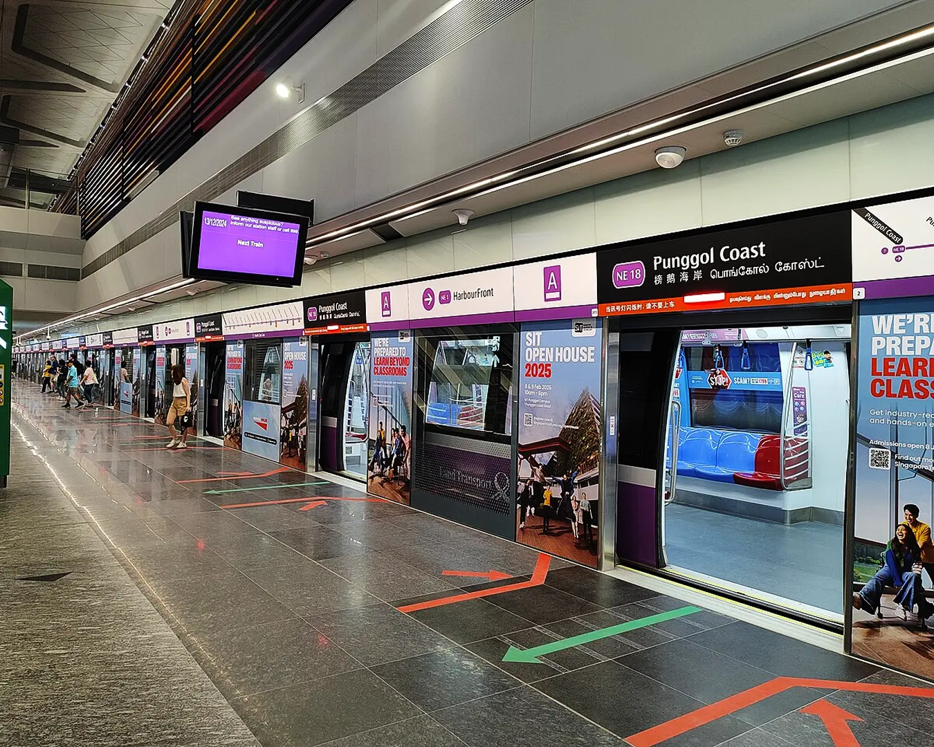 Interior of a North-East Line MRT station platform with commuters waiting near the tracks and clear station signage overhead