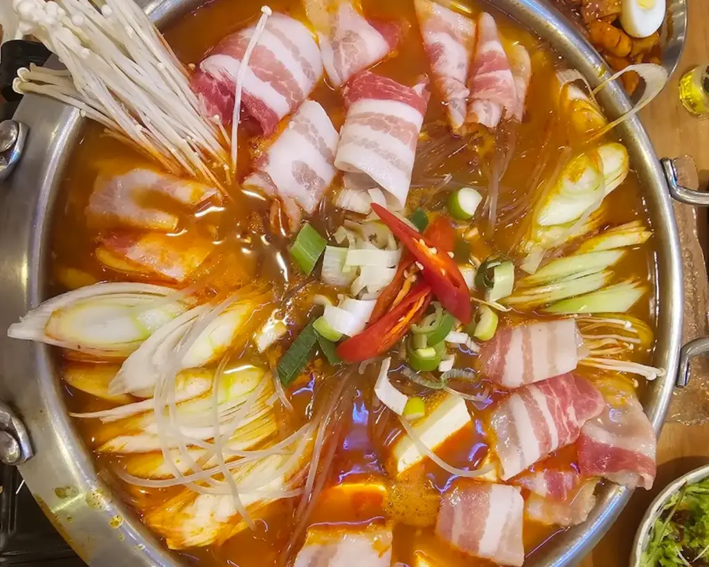 A bubbling Korean steamboat filled with sliced meats, vegetables, and noodles cooking in a rich broth, perfect for communal dining and a warm, comforting meal.