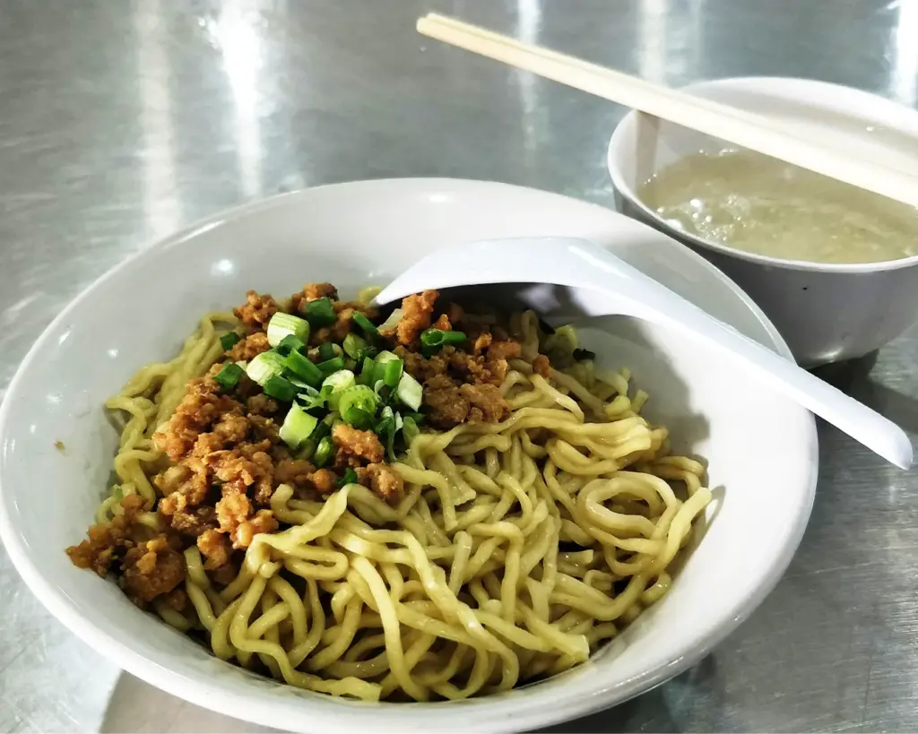 A bowl of savoury minced meat noodles topped with minced pork, sliced mushrooms, and leafy greens, a classic Singapore hawker dish known for its rich sauce and comforting flavours.