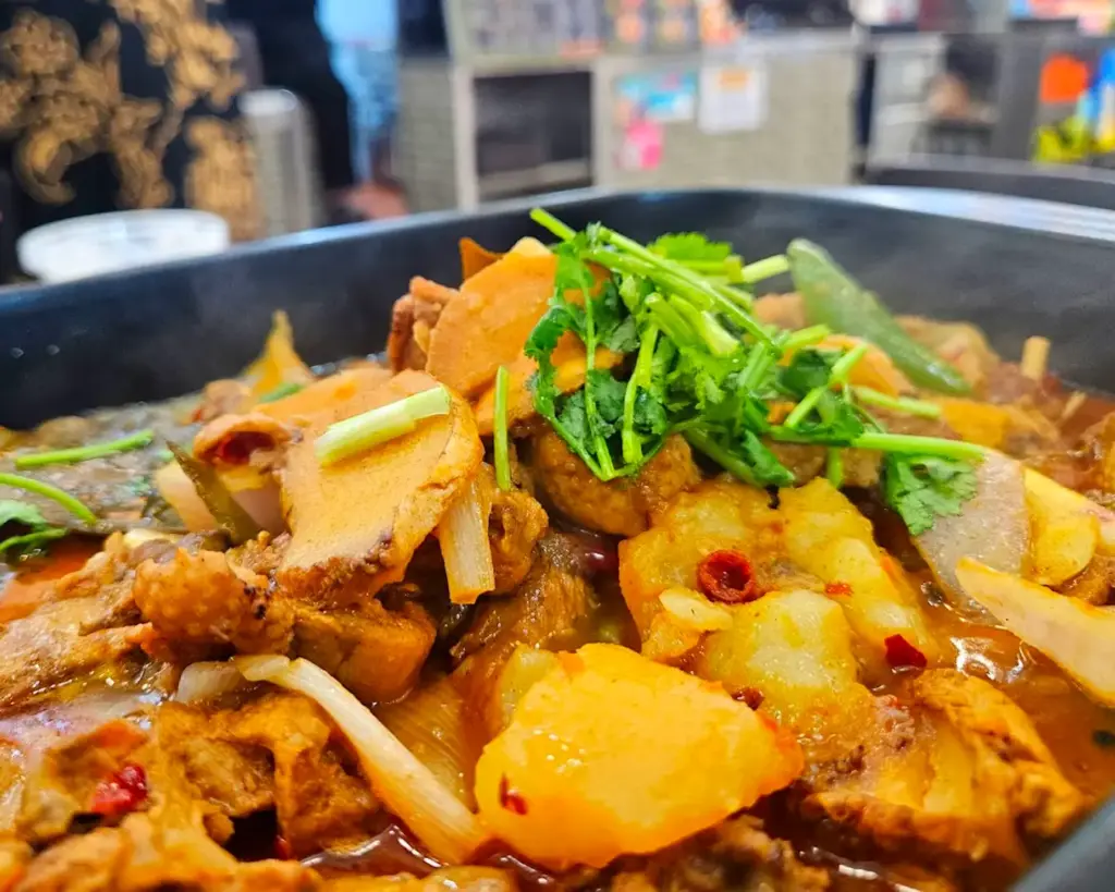 A hearty bowl of bak chor mee topped with minced pork, noodles, and chilli sauce, glistening with a spicy kick, served with soup on the side in a casual hawker-style setting.
