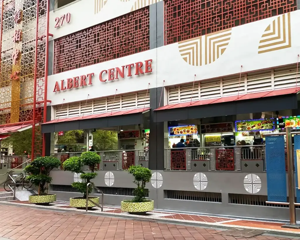 The entrance of Albert Centre Market & Food Centre, showing a mix of diners gathering around. The setting highlights a traditional local marketplace vibe, blending fresh produce stalls with popular food vendors.