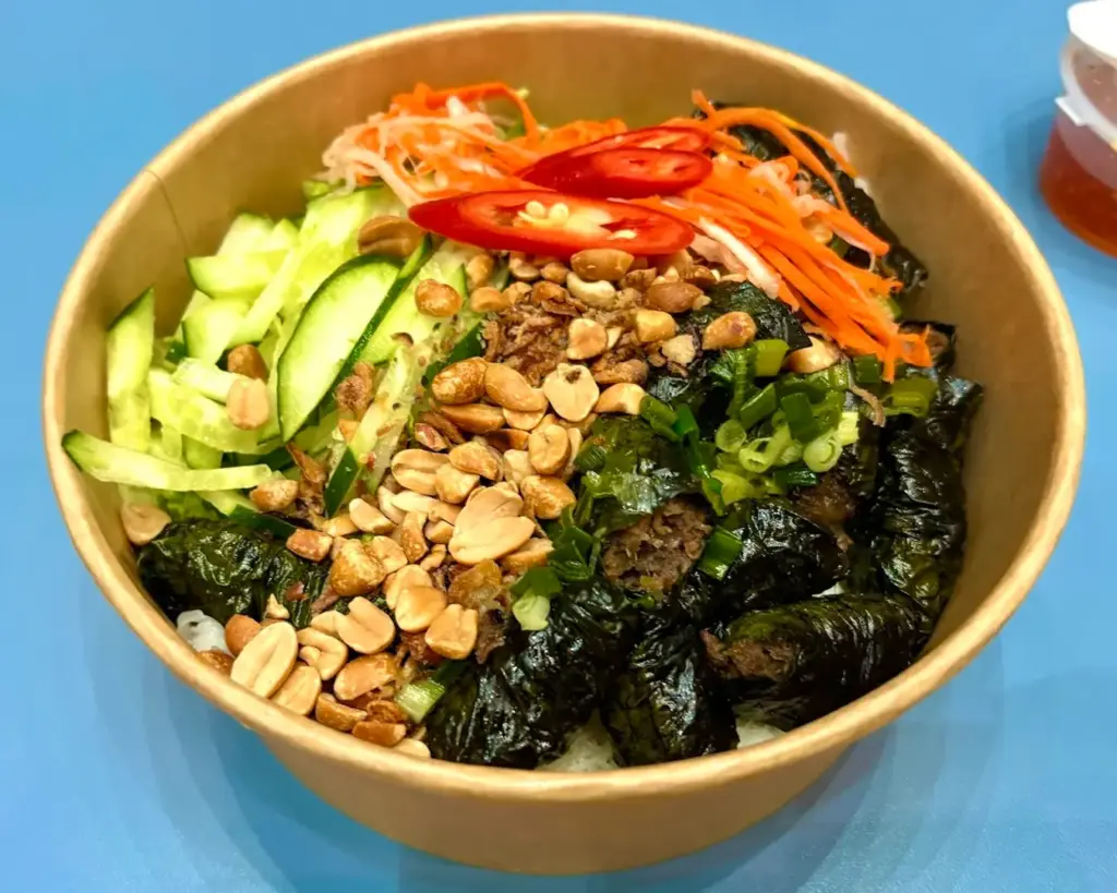 A vibrant bowl of Vietnamese cuisine filled with fresh herbs, noodles, and spiced meat, showcasing a balance of colours and textures with a fragrant, savoury appeal.