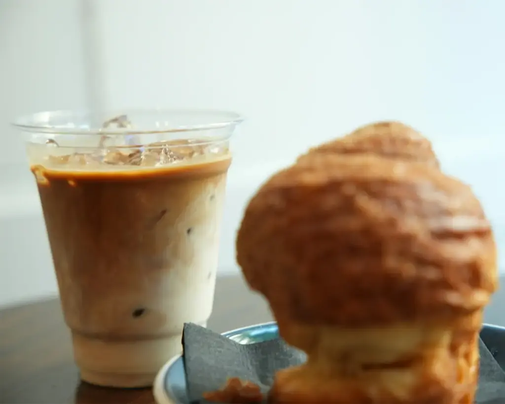 A refreshing iced coffee served in a clear glass alongside a selection of pastries, arranged neatly on a table in a cosy café setting.