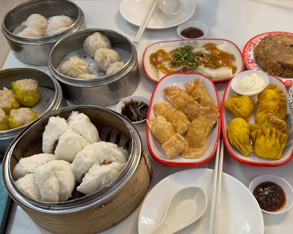 A table filled with assorted dim sum dishes, including dumplings, buns, and rolls, neatly arranged in bamboo steamers and plates, perfect for a shared dining experience.