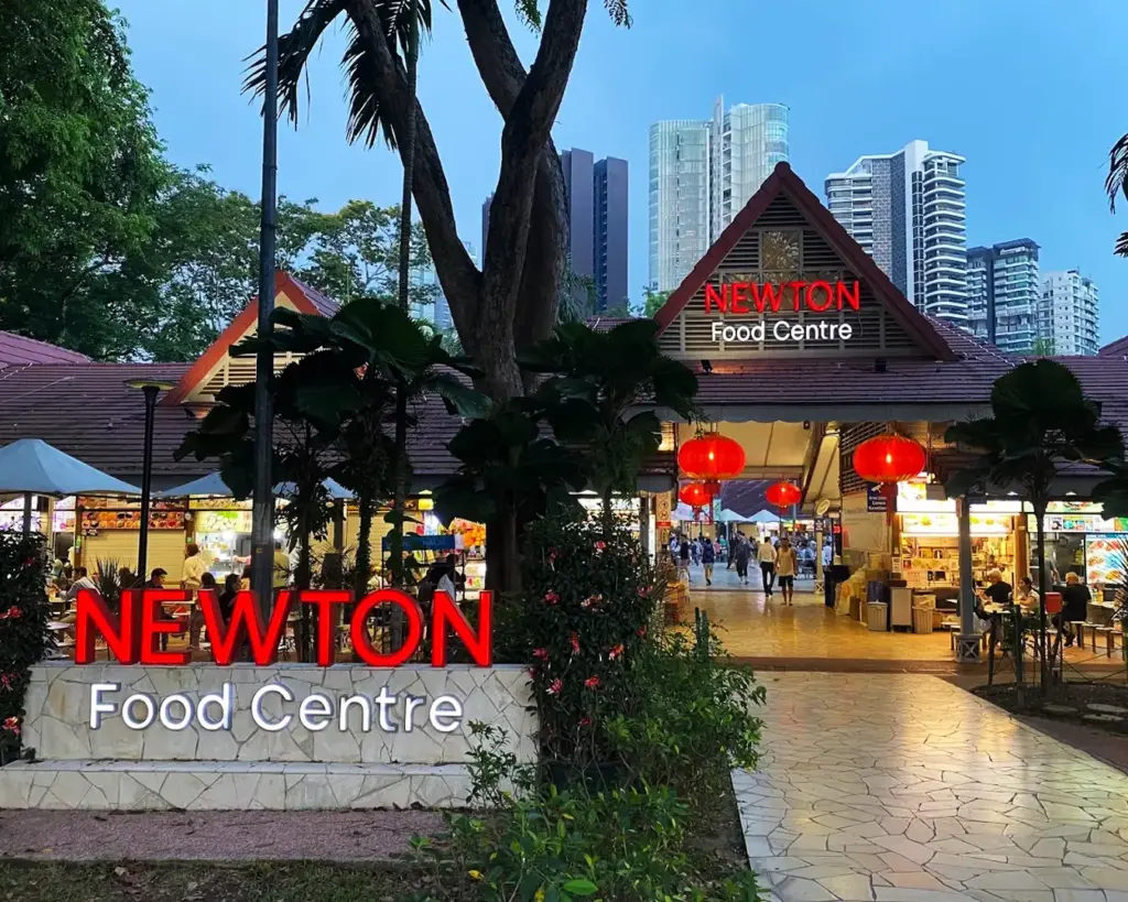 Newton Food Centre in Singapore, a vibrant open-air hawker centre filled with food stalls, bright signage, and diners enjoying local street food.