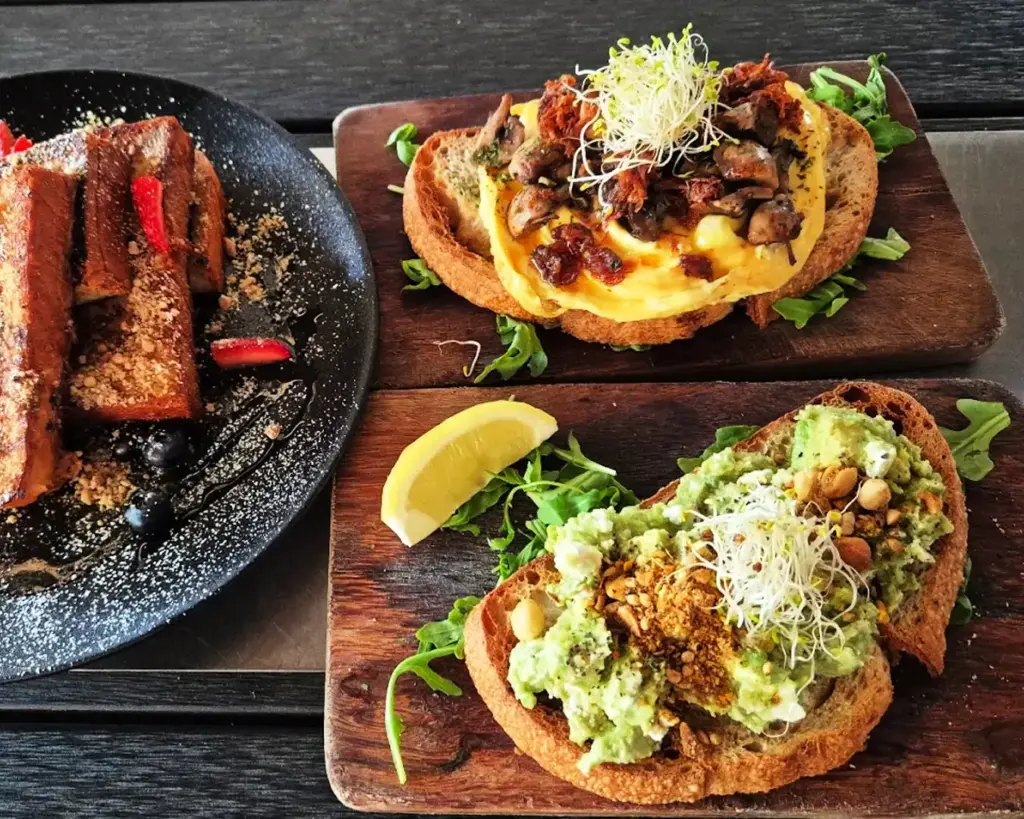 Thick slices of toasted focaccia bread filled with tender duck confit, crispy candied bacon, and melted cheese. The sandwich looks rich and hearty, with layers of savoury flavours packed between the golden, slightly crisp bread.