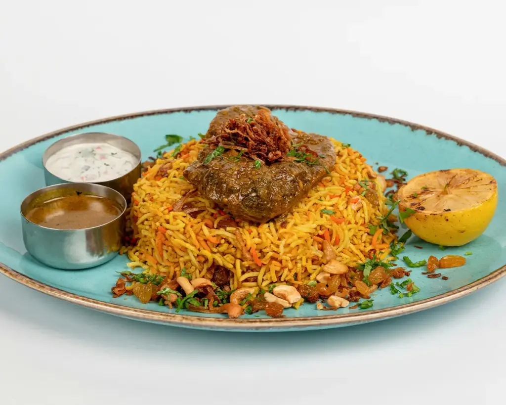 A plate of fragrant briyani rice served with spiced meat, curry gravy, and traditional accompaniments such as pickles and vegetables.