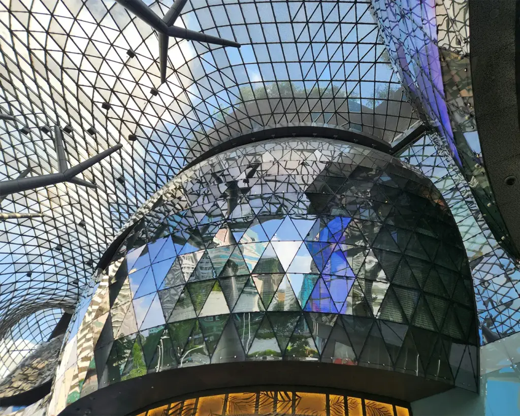 Exterior of ION Orchard shopping mall in Singapore with its iconic futuristic glass façade and luxury storefronts along the busy Orchard Road.