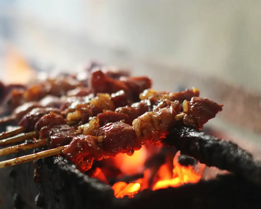 Skewers of satay grilling over charcoal flames, with smoke rising as the meat cooks and develops a rich, smoky aroma.