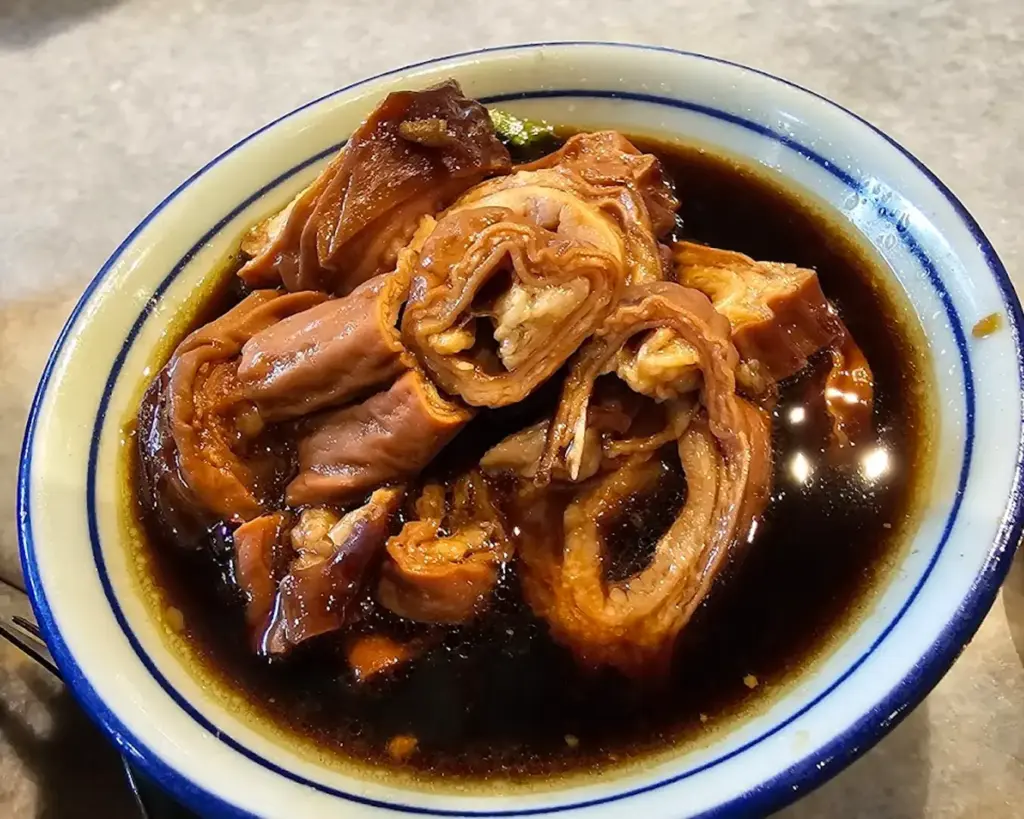 A steaming bowl of bak kut teh featuring tender pork ribs simmered in a herbal broth, accompanied by rice and side dishes in a cosy dining setting.