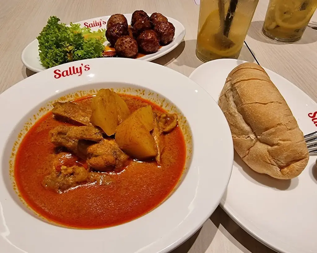 A rich serving of curry chicken with tender pieces in thick gravy, paired with a hearty roti john filled with egg and meat, representing bold local flavours.
