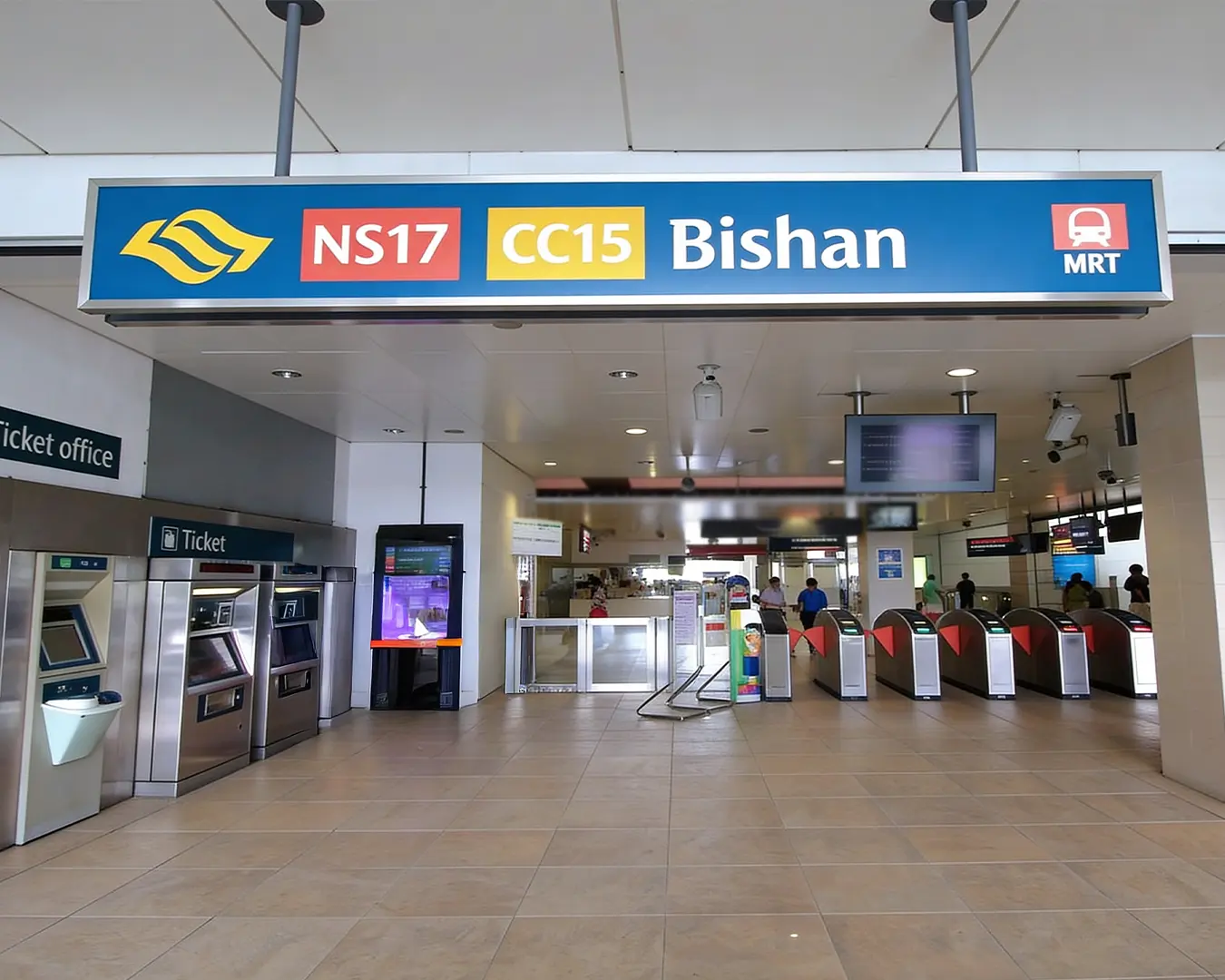 The main entrance area of Bishan MRT station featuring the station signage, with commuters walking nearby and surrounding urban structures.