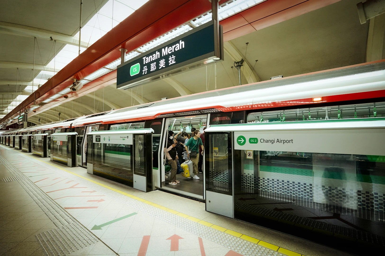 Singapore MRT train at Tanah Merah station with passengers boarding, platform screen doors open, and sign showing Changi Airport direction in a clean, modern transit setting.