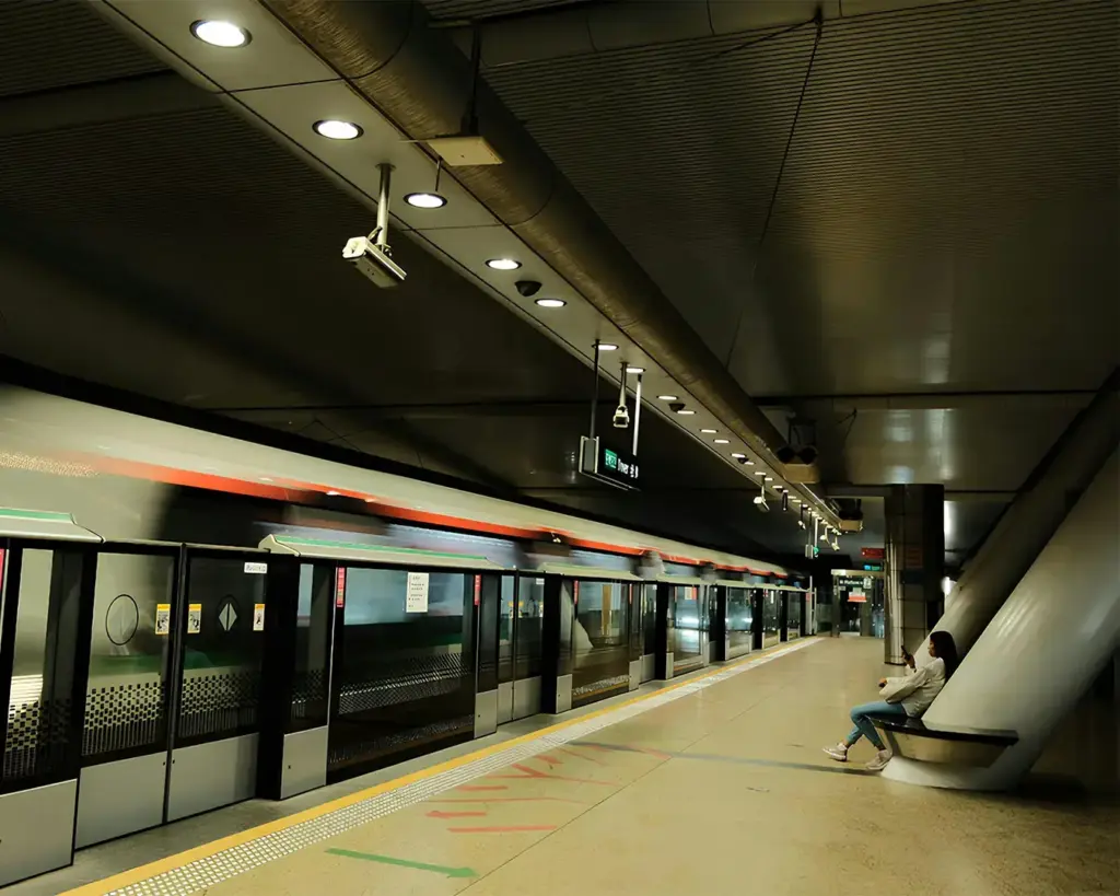 A quiet, modern subway platform with a single person sitting on a bench. The sleek, lit interior creates a calm, spacious atmosphere.
