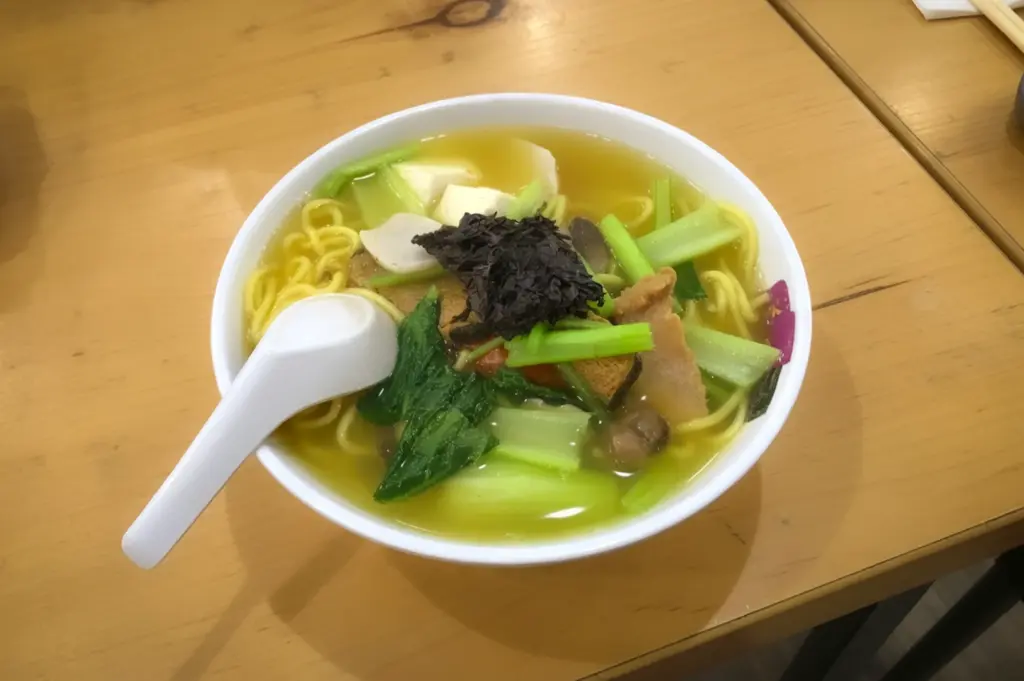Savory bowl of dry tossed Asian noodles topped with minced meat, crispy ikan bilis, and fresh greens, served in a traditional patterned ceramic bowl for an authentic local dining experience.