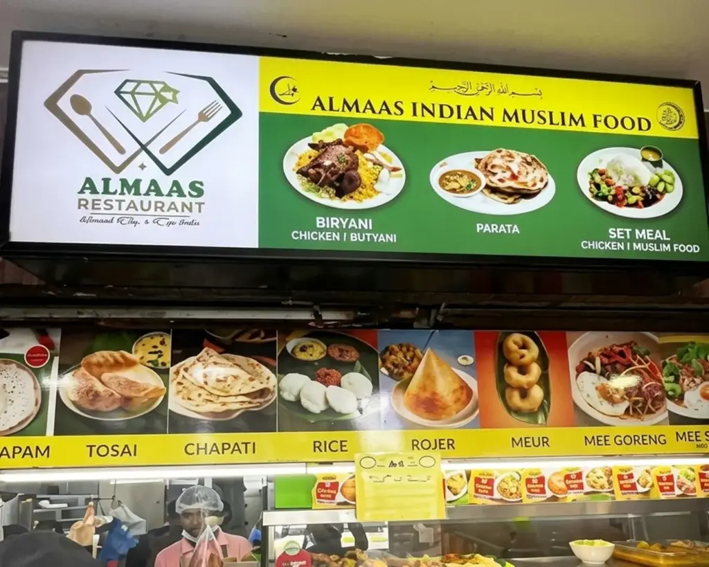 Alt text: "Almaas Restaurant sign displaying Indian Muslim dishes like biryani, parata, and set meals. Below are images of traditional foods like tosai and chapati."