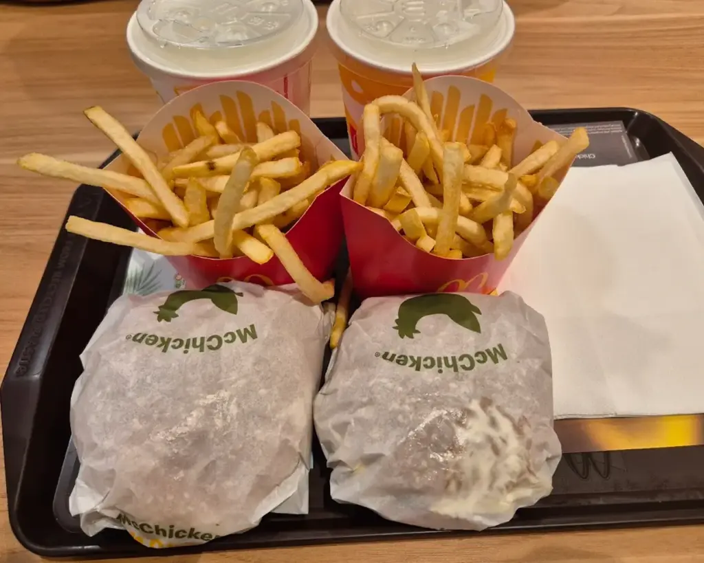 A tray with two McChicken sandwiches wrapped in paper, two servings of fries in red cartons, and two drinks with white lids on a wooden table.