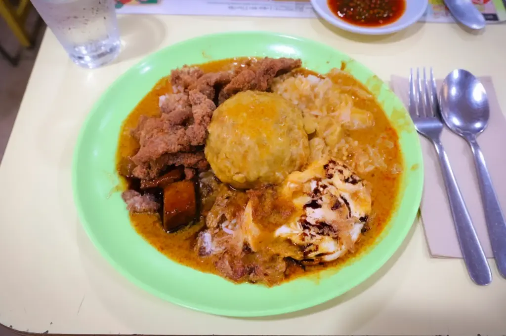 Authentic plate of Hainanese curry rice topped with thick savory gravy, featuring crispy pork chop, a fried egg, and stewed cabbage, representing a classic Singaporean hawker comfort food.