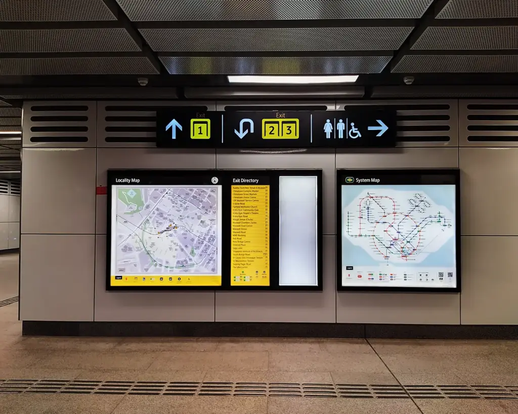 Subway station wall with illuminated maps and exit signs. Arrows indicate directions. Maps detail local area and transit system. Modern and organized setting.