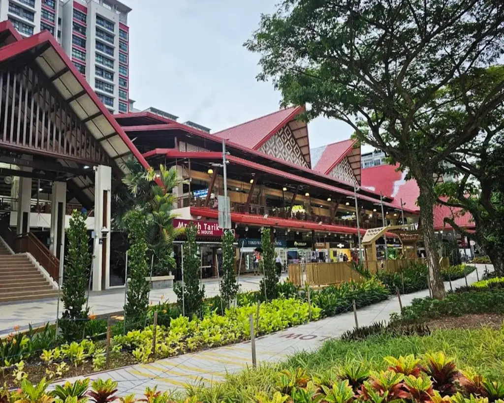 A vibrant hawker center with red roofs, nestled among lush greenery and framed by a large tree, conveys a lively and welcoming atmosphere.