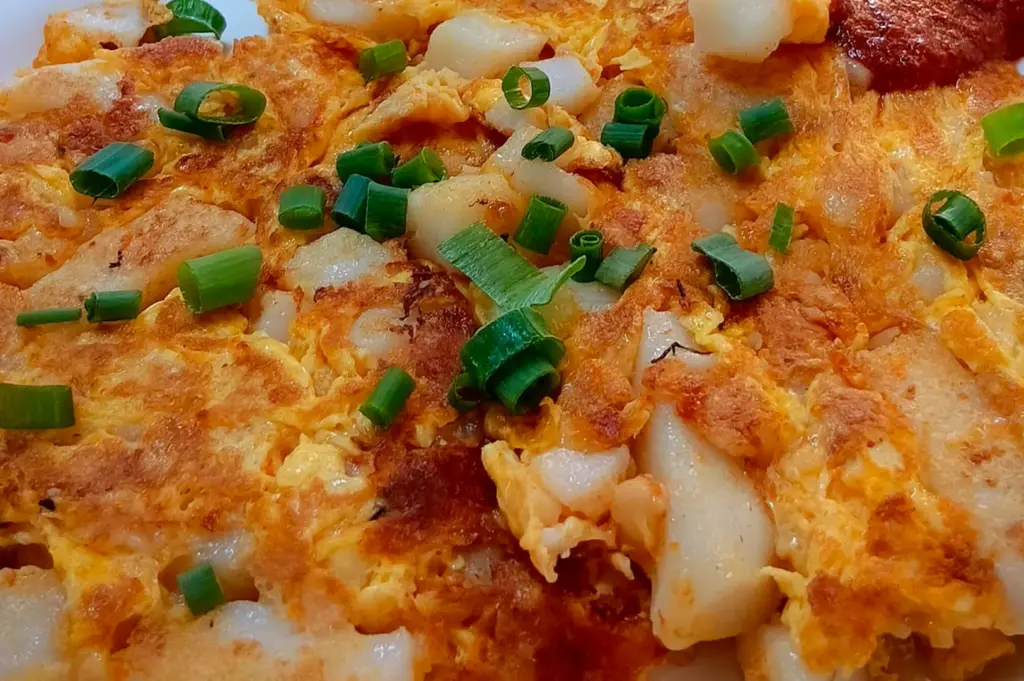 Savory "white" Chai Tow Kway (Fried Carrot Cake) featuring stir-fried radish cubes bound together with a crispy egg omelette, garnished with fresh spring onions and a side of chili for an authentic Singaporean hawker experience.