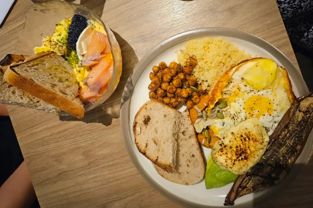 Hearty Mediterranean and brunch dishes from Penny University in Singapore, featuring a main plate with shakshuka-style eggs, grilled halloumi, avocado, and spiced chickpeas, alongside a bowl of creamy scrambled eggs topped with smoked salmon and caviar served with toasted sourdough.