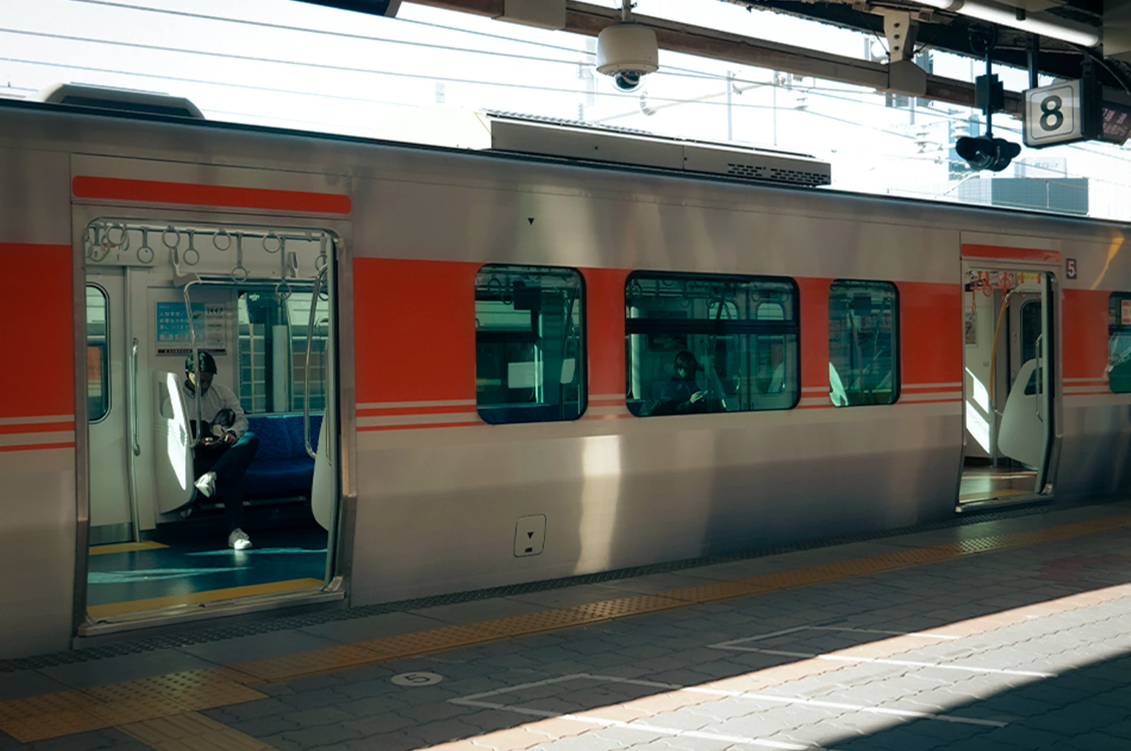 Modern silver and orang commuter train stopped at a sunny platform. View of open doors, passengers sitting and station markings.