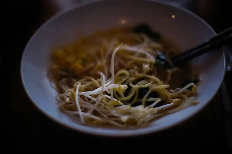Close-up of a bowl of Asian noodle soup with bean sprouts, chopsticks, and dark moody lighting in a cozy restaurant setting