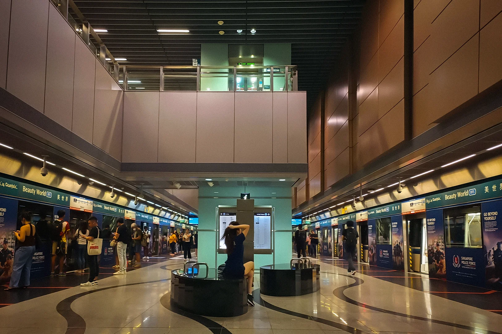 Interior platform view of Beauty World MRT Station in Singapore featuring commuters waiting beside train doors, modern architecture, and bright underground transit lighting
