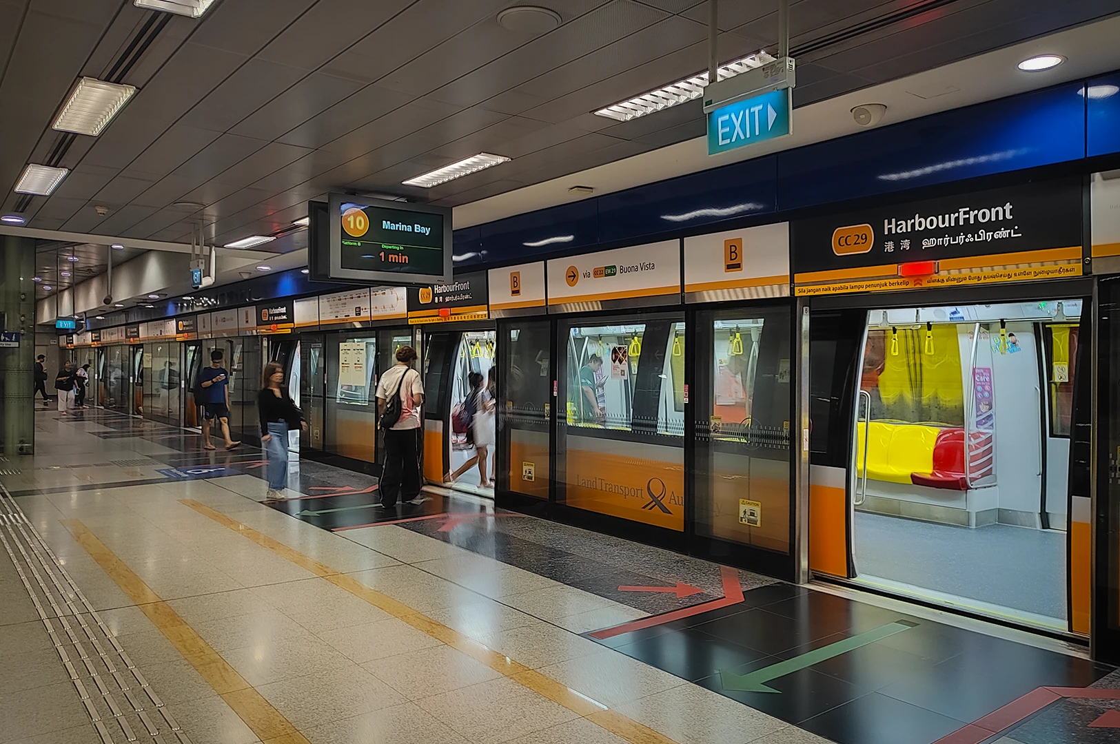 Passengers boarding a train at HarbourFront MRT station platform in Singapore, with clear signage, platform screen doors, and directional floor markings.