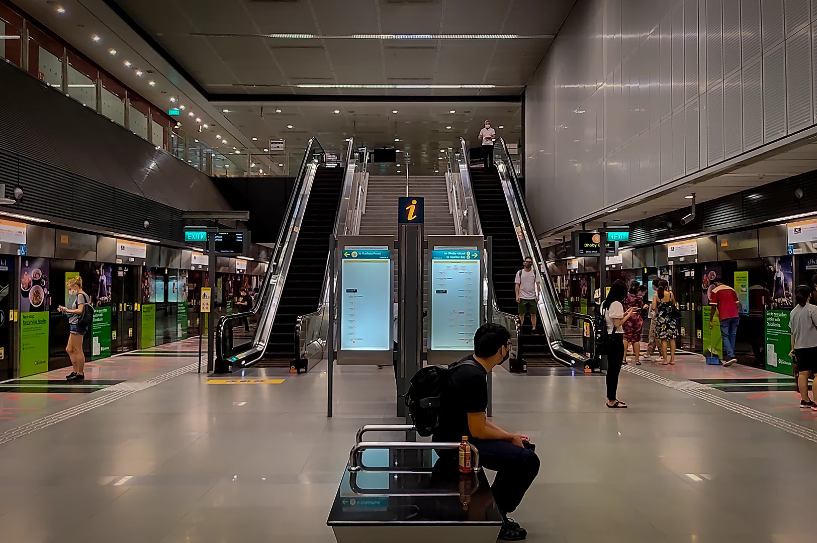 Wide view of Holland Village MRT station platform in Singapore featuring escalators, commuters, platform screen doors and modern underground Circle Line station architecture under bright lighting