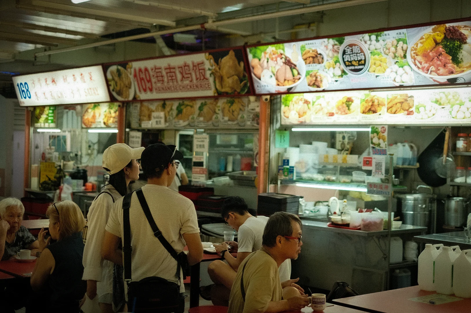 Busy Singapore hawker centre with diners seated at tables and local food stalls serving chicken rice and other traditional dishes under bright signboards