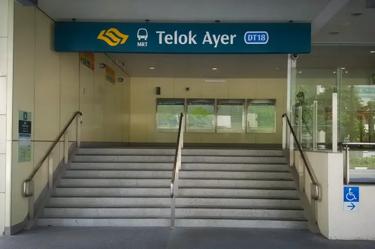 Entrance to Telok Ayer MRT Station Exit A in Singapore featuring station signage, stair access, glass walls, and modern urban transit architecture