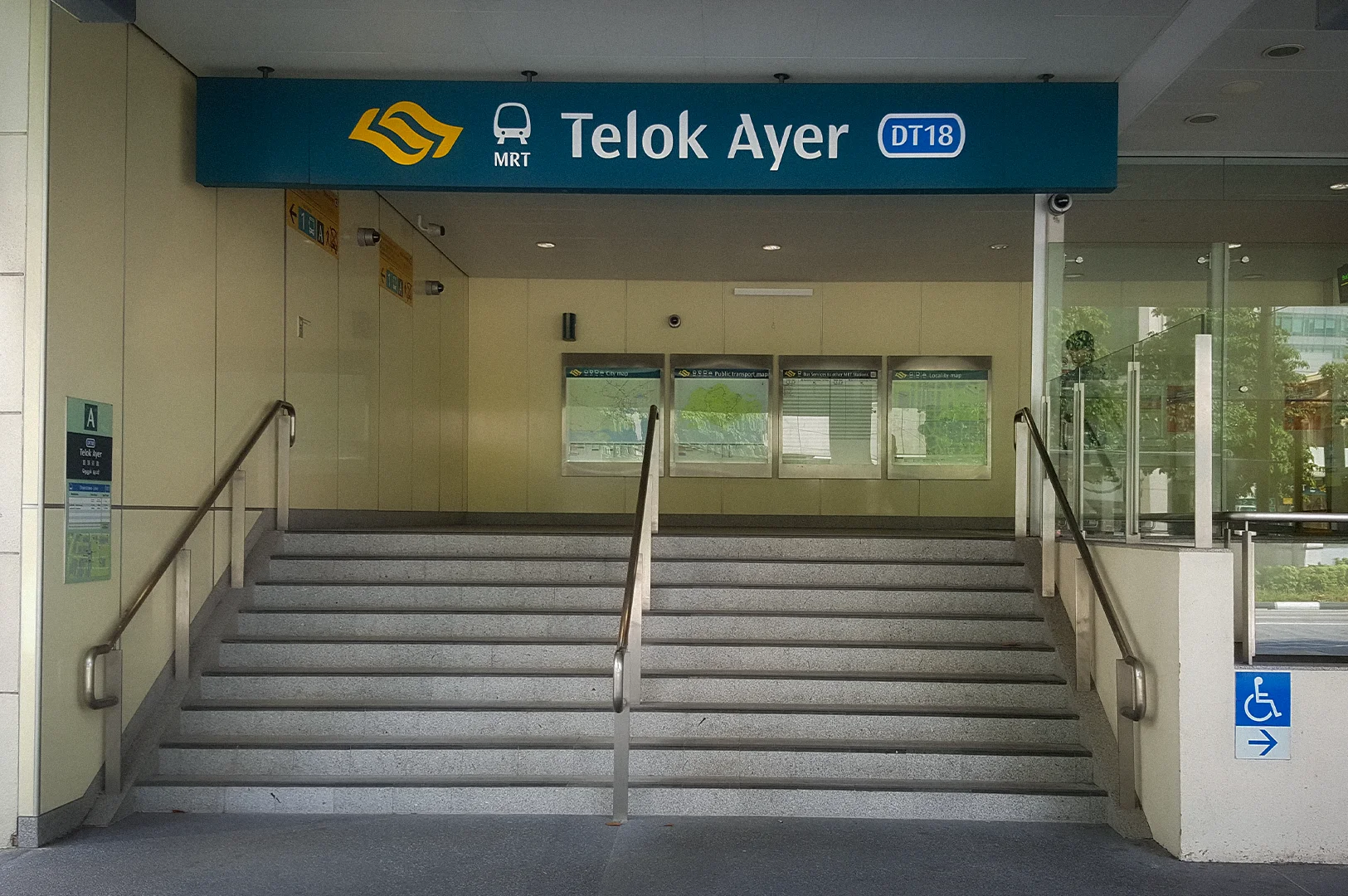 Entrance to Telok Ayer MRT Station Exit A in Singapore featuring station signage, stair access, glass walls, and modern urban transit architecture