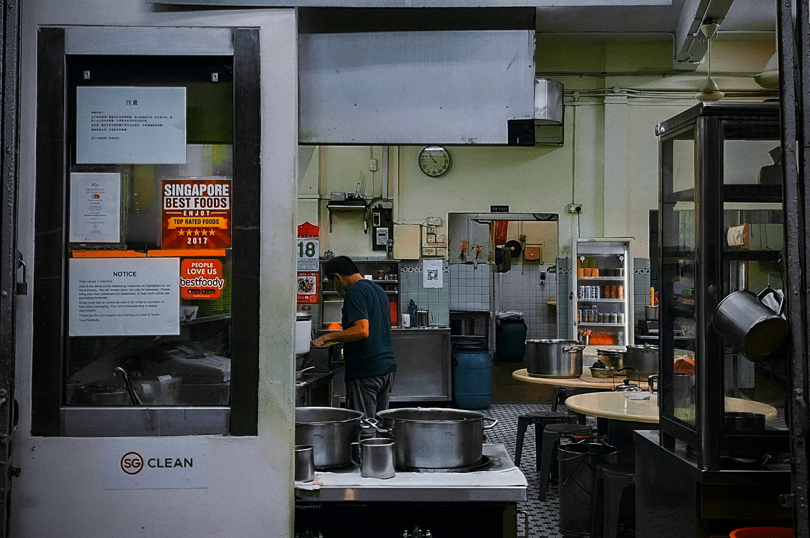 Traditional Singapore hawker stall kitchen with Chinese signage, stainless steel cooking equipment, and staff preparing food inside a local eatery interior