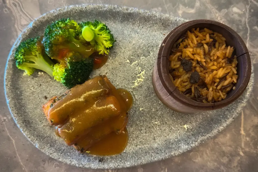 Gourmet vegetarian meal at Elemen Singapore featuring broccoli, savory sauce-covered rolls, and seasoned rice served on a modern stone plate over a marble table surface