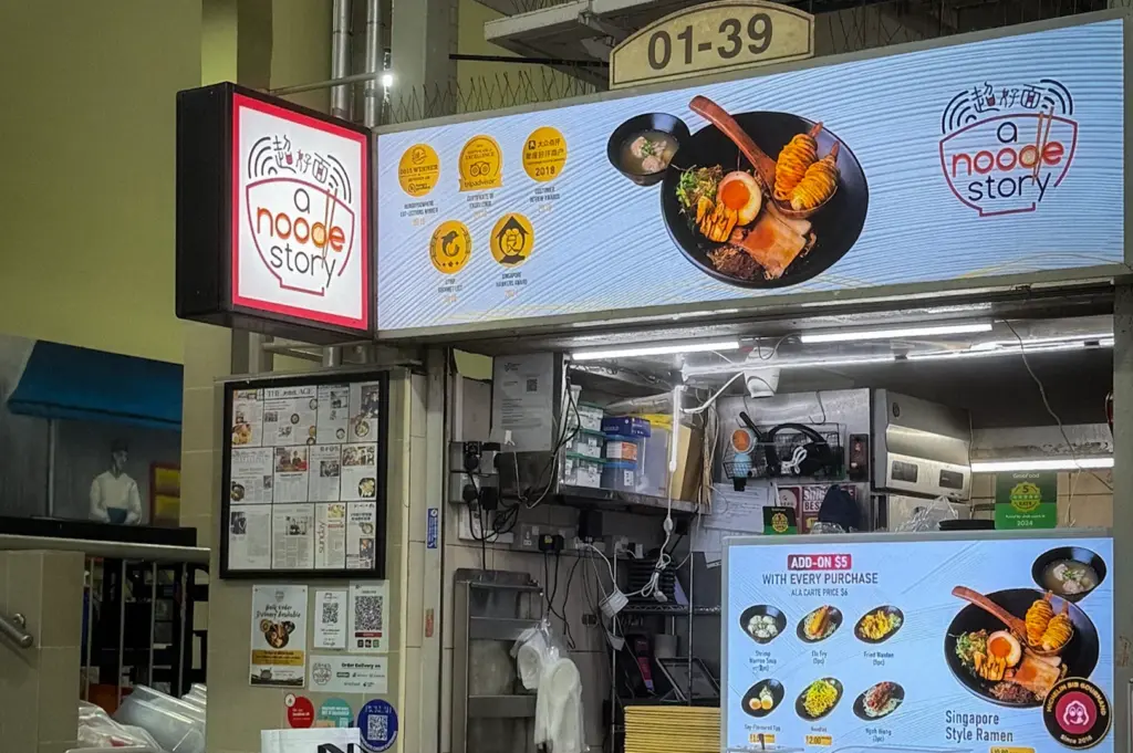 Noodle Story ramen hawker stall at a Singapore food centre featuring illuminated menu signage, casual dining tables, and Singapore-style ramen dishes on display