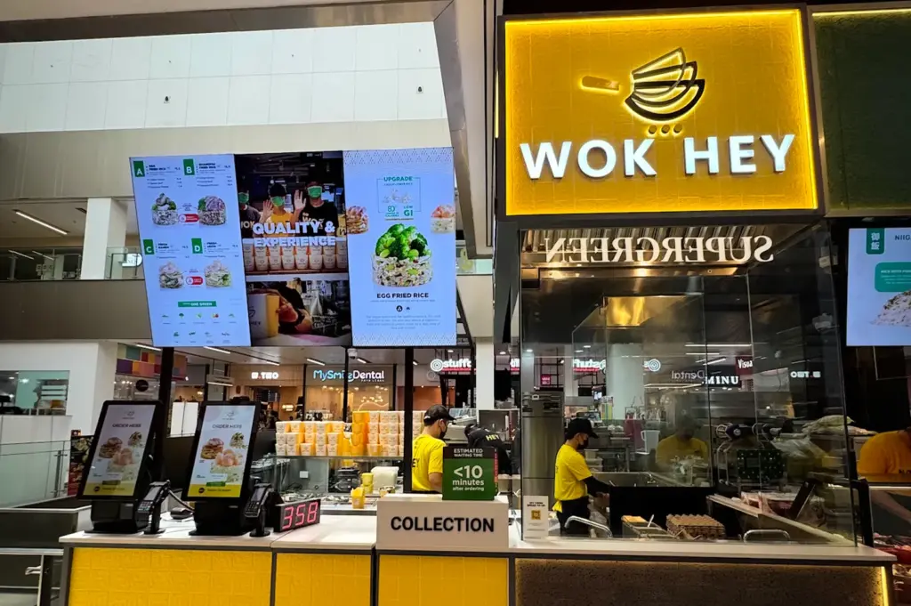 Wok Hey takeaway kiosk in Singapore shopping mall serving freshly cooked fried rice and noodle dishes with illuminated menu boards and open kitchen counter visible