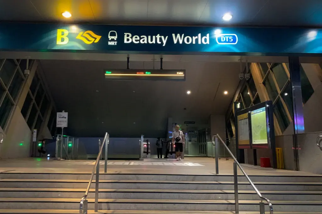 Commuters boarding and exiting trains at Beauty World MRT Station DT5 platform in Singapore with escalators, platform screen doors, and station signage visible indoors