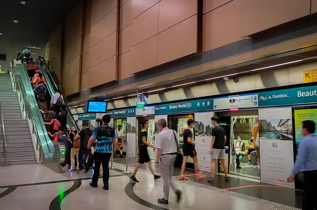 Commuters boarding and exiting trains at Beauty World MRT Station DT5 platform in Singapore with escalators, platform screen doors, and station signage visible indoors