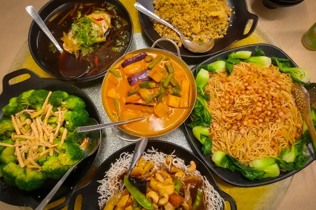 Large spread of vegetarian zi char dishes at Nature Vegetarian Delights Singapore featuring curry vegetables, fried noodles, broccoli, crispy noodles, tofu soup, and mixed mushroom dishes on a round dining table