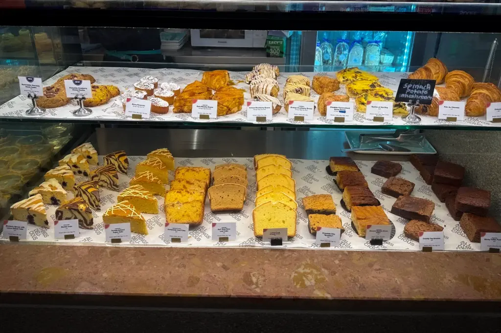 Pastry and dessert display at All Things Delicious Singapore featuring croissants, scones, quiches, brownies, loaf cakes, cookies, and assorted baked goods inside a cafe glass counter display