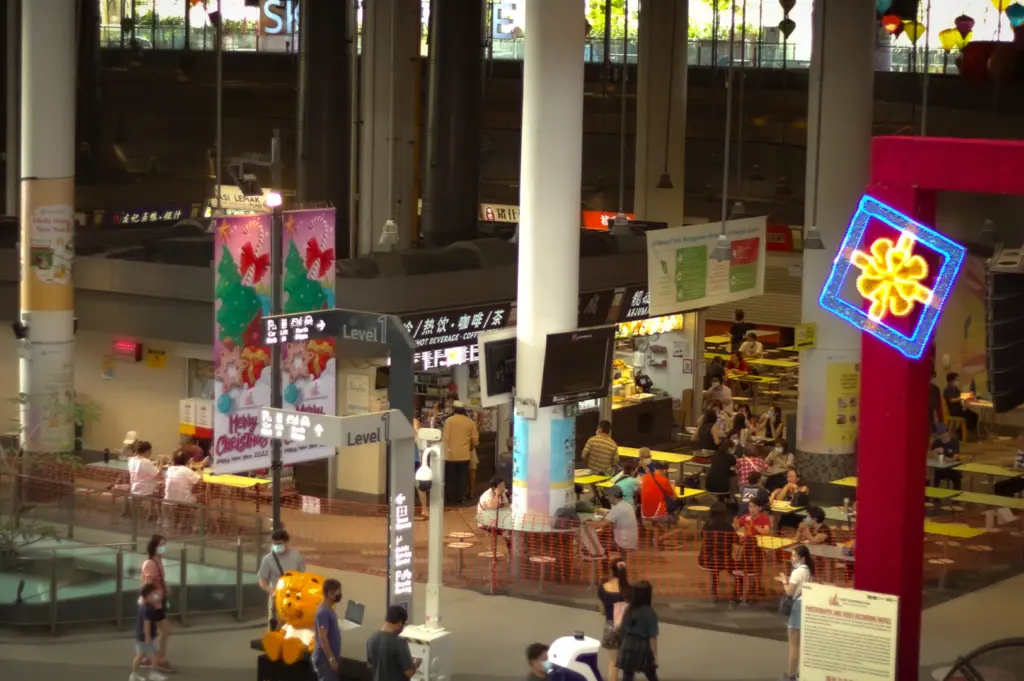 Interior of Our Tampines Hub hawker centre in Singapore with diners at tables, food stalls, festive decorations, and signage across multiple levels.