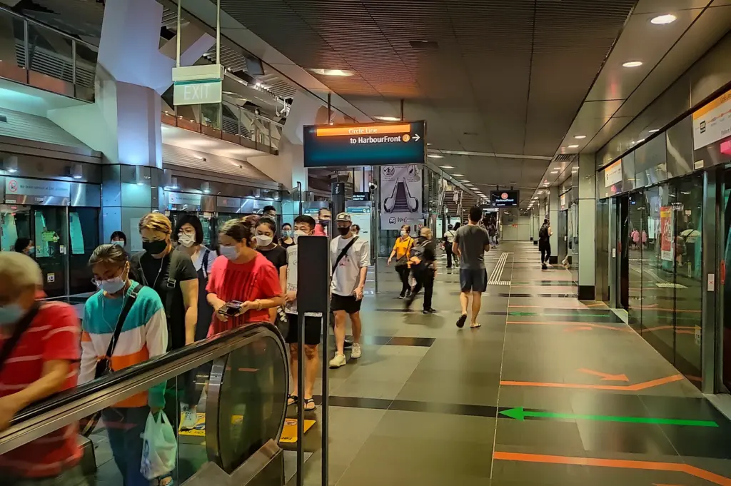 Commuters walking along Paya Lebar MRT Circle Line platform in Singapore with directional signage to HarbourFront, platform screen doors and escalator access visible inside the station