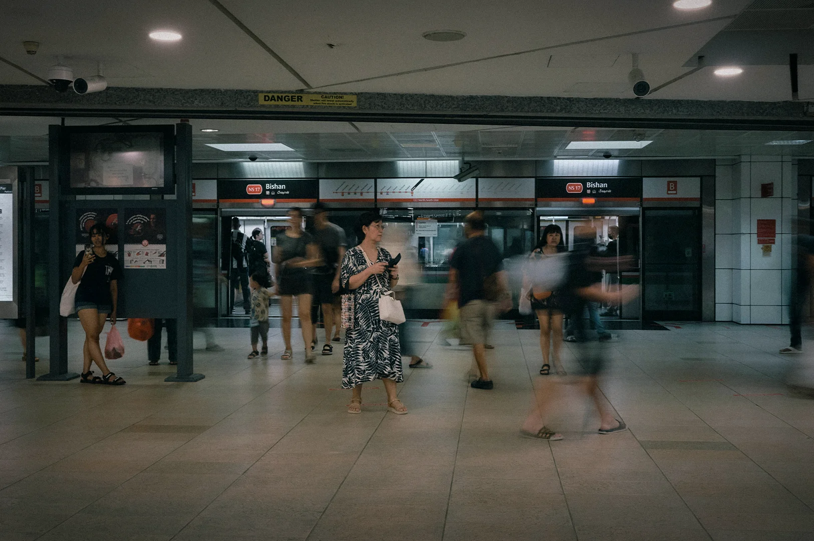 Commuters moving through the concourse of Bishan MRT Station in Singapore, with station signage, platform screen doors, and motion blur capturing the busy pace of daily public transport travel.