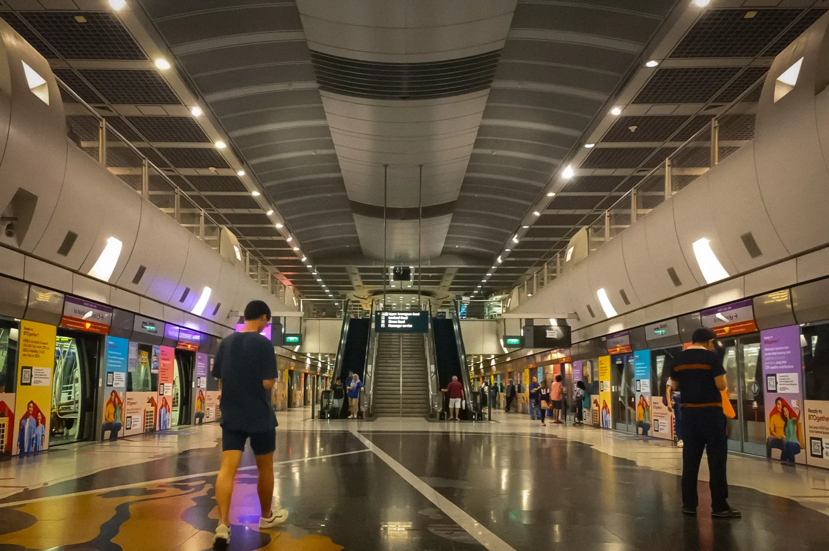 Wide view of Kovan MRT Station platform in Singapore, featuring modern architecture, train doors, escalators, and commuters waiting for public transportation.