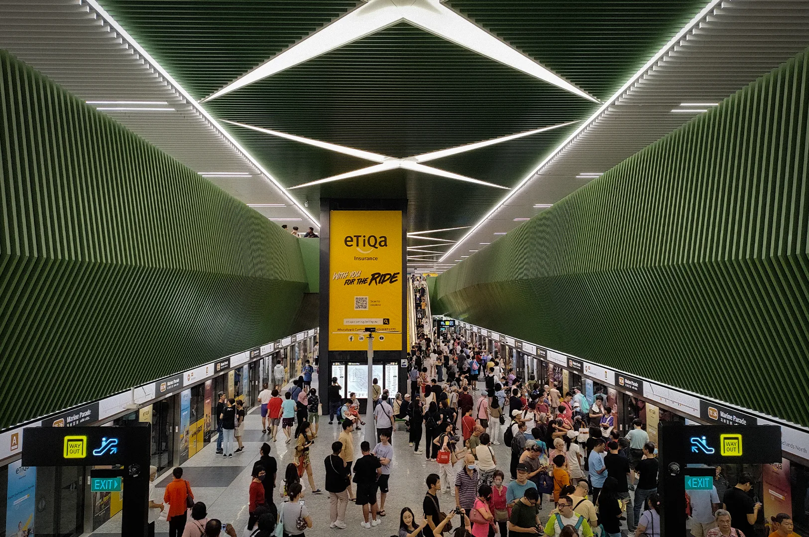 Marine Parade MRT Station on Singapore's Thomson-East Coast Line, featuring modern underground platforms, geometric ceiling lighting, platform screen doors, and commuters during peak travel hours.