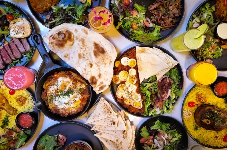 Overhead view of a large Middle Eastern feast featuring grilled meats, biryani rice, fresh salads, flatbreads, eggs, and colorful beverages served on a dining table in Gyeongju.