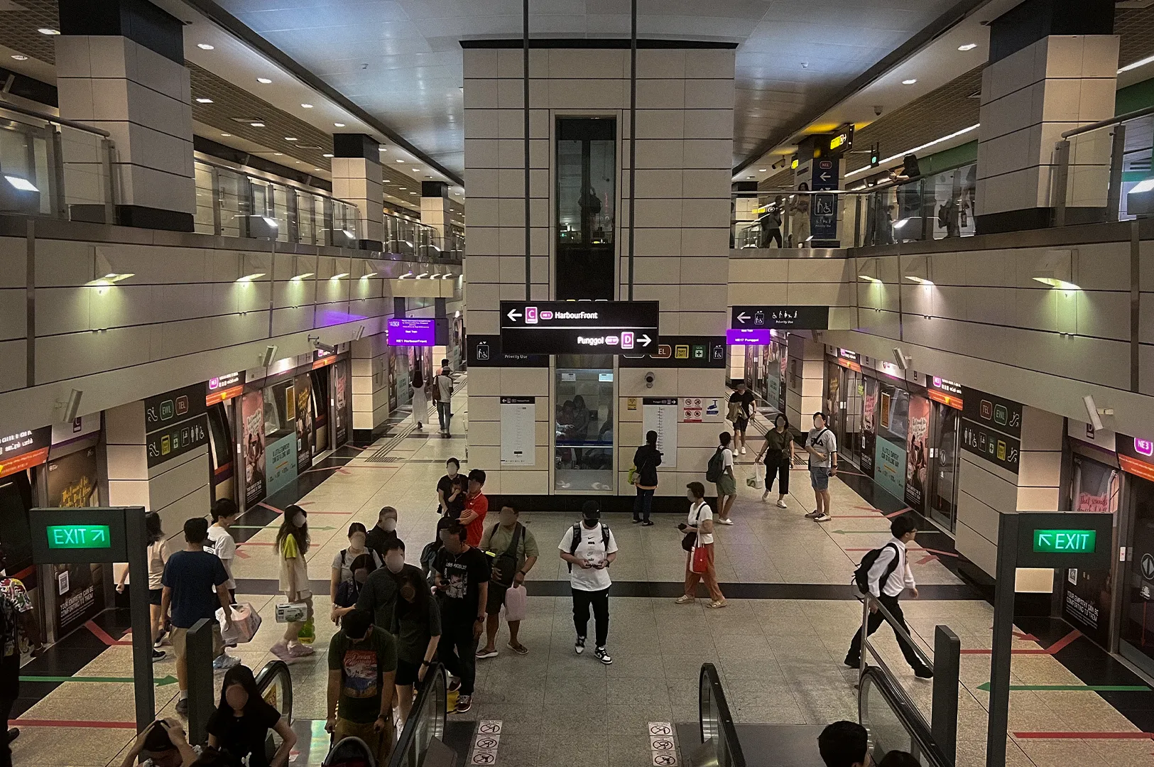 Busy North East Line MRT station platform in Singapore with passengers using escalators and waiting areas, featuring modern underground architecture, platform screen doors, directional signage, and multiple train boarding platforms.